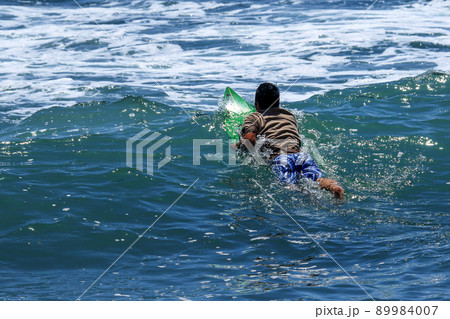 湘南海岸鎌倉稲村ケ崎の海で、よい波を求めて沖に漕ぎ出すサーファー 89984007