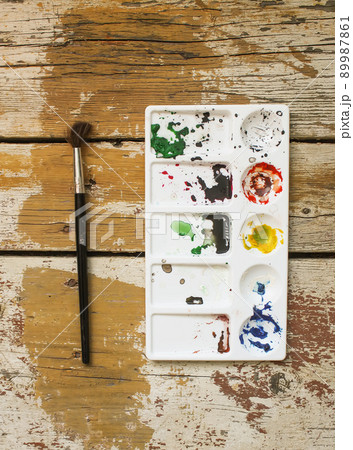 Palette with paints stains and watercolor brush on wooden background. Palette with paints stains and watercolor brush on wooden background. 89987861