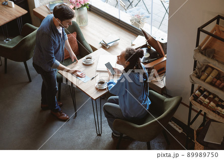 Young pretty smiled woman sitting at table with coffee in cafe and man coming for meeting. Young pretty smiled woman sitting at table with coffee in cafe and man coming for meeting. 89989750