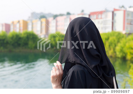 A Muslim woman in a black outfit walks through the city covering her face with a burqa 89989897