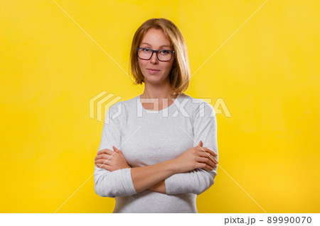 Young blonde woman in glasses posing with her arms crossed. Yellow background. Copy space Young blonde woman in glasses posing with her arms crossed. Yellow background. Copy space 89990070