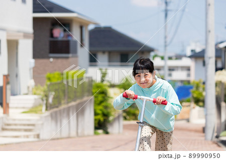 夏の名古屋の住宅地でスクーターを遊んでいる可愛い小学生の女の子の姿 89990950