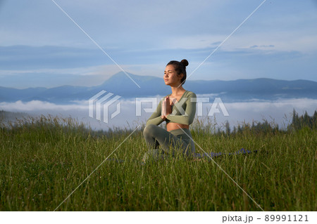 Sporty young woman sitting on yoga mat with namaste gesture and enjoying outdoors meditation. Concept of wellness, spirituality and harmony. Sporty young woman sitting on yoga mat with namaste gesture and enjoying outdoors meditation. Concept of wellness, spirituality and harmony. 89991121
