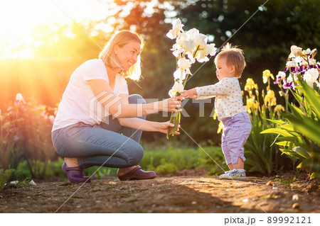 Happy mother gives a bouquet of irises to her cute baby. Sunset light in the garden. The concept of March 8 and Happy Children's Day 89992121