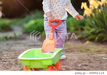 Happy children's day. Toddler playing with a plastic toy cart at the summer garden. Close up. Concept of gardening 89992124