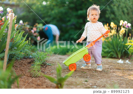 Adorable baby playing with a plastic toy cart at the garden. Parents blurred on the background. Concept of summertime 89992125