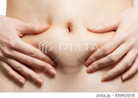 A woman holds her hands to her stomach, pulling the skin with fat. Close-up of the abdomen and navel. The concept of obesity, weight loss and liposuction A woman holds her hands to her stomach, pulling the skin with fat. Close-up of the abdomen and navel. The concept of obesity, weight loss and liposuction 89992659