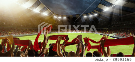 Victory. Back view of football, soccer fans cheering their team with scarfs at crowded stadium at evening time. Concept of sport, competition. Out of focus effect 89993169