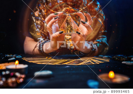 Sorcery. The witch held a glowing pyramid in her hands and conjured it. The tarot cards were on the table. Hands close-up. The concept of divination and astrology 89993465