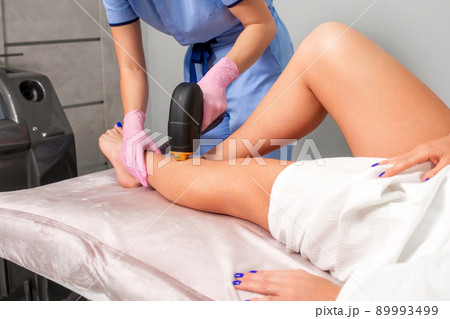 Cosmetologist in medical pink gloves removes hair with laser epilation to the client's legs. The concept of professional apparatus epilation in a beauty salon 89993499