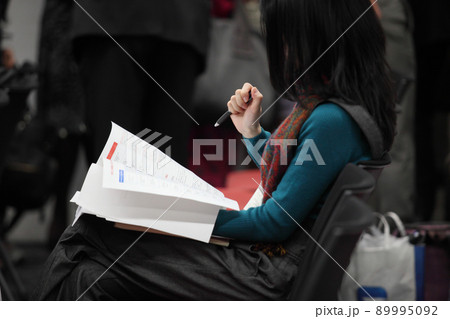 イスに座って資料の紙とペンを持つ女性の上半身 89995092
