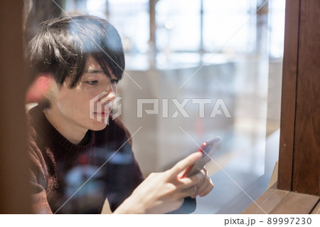 カフェの窓辺でスマートフォンを操作する20代男性 カフェの窓辺でスマートフォンを操作する20代男性 89997230