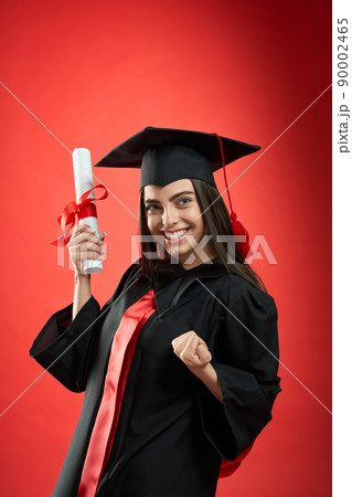 Front view of pretty young female holding diploma. Girl smiling, looking at camera, showing hurray, wearing graduate gown and mortarboard. Concept of education and youth. Front view of pretty young female holding diploma. Girl smiling, looking at camera, showing hurray, wearing graduate gown and mortarboard. Concept of education and youth. 90002465