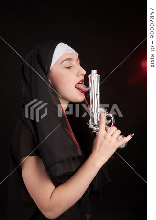 Young nun sister holds silver revolver up and licking it. Young nun sister holds silver revolver up and licking it. 90002857