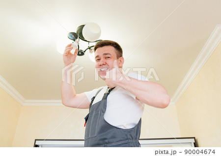 A male electrician changes the light bulbs in the ceiling light.  90004674