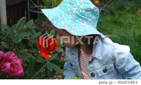 Happy Preschool little girl kid Daughter wear works gloves humic boots smelling scent of flowers tulips in garden. Helping mother ouside Nature gardering planting environmental Spring Summer concept. 90005863