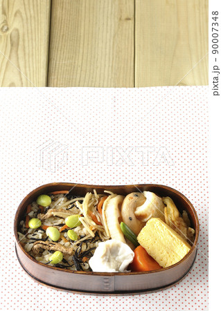 ひじきと枝豆のご飯、シュウマイや玉子焼き、煮物等たくさんのおかずが入っている幕の内弁当を俯瞰で撮影 90007348