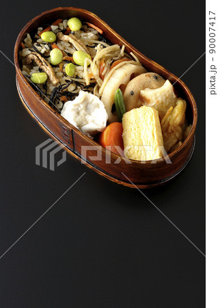 ひじきと枝豆のご飯、シュウマイや玉子焼き、煮物等沢山のおかずが入っている幕の内弁当を黒背景で俯瞰撮影 90007417