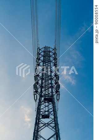 見上げる送電鉄塔の上部と高圧線と雲が少ない青空　タテ 暖色寒色強調 90008554