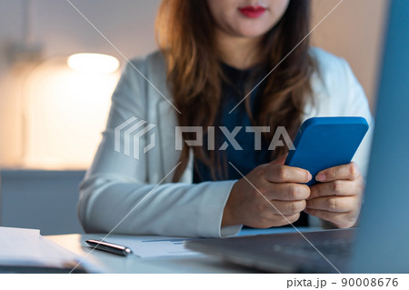 Overwork Concept The female office employee who wears white blazer working late at the office while texting her phone to someone Overwork Concept The female office employee who wears white blazer working late at the office while texting her phone to someone 90008676