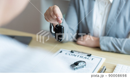 Insurance concept the car dealer explaining the conditions of the car while showing a car key to his client 90008698
