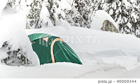 Stunning mountain landscape with green tourism tent on snow, covered snowstorm in winter against backdrop of coniferous trees. Stunning mountain landscape with green tourism tent on snow, covered snowstorm in winter against backdrop of coniferous trees. 90009344