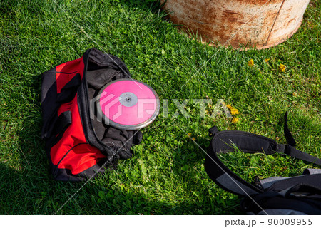Red athletic equipment bag on the grass with pink track and field discus Red athletic equipment bag on the grass with pink track and field discus 90009955