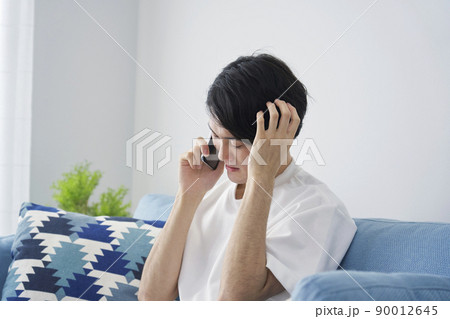 リビングでスマホを持って頭を抱える男性 リビングでスマホを持って頭を抱える男性 90012645