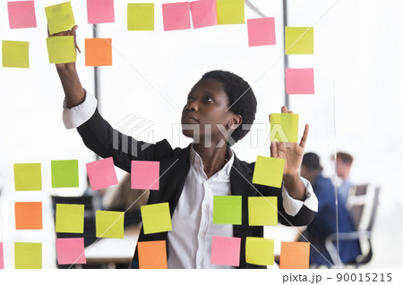 African businesslady jotting on adhesive stickers attached on glass wall 90015215