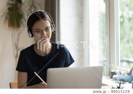 Focused positive young student girl in eyeglasses, headphones writing notes Focused positive young student girl in eyeglasses, headphones writing notes 90015229
