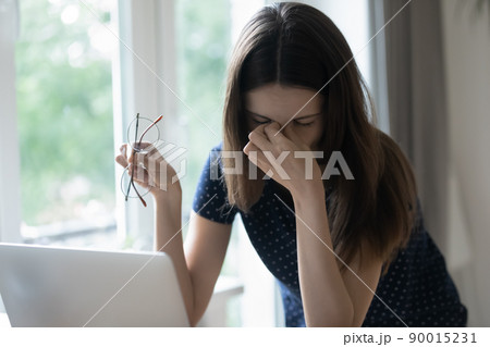 Tired freelance employee girl sitting at table with computer Tired freelance employee girl sitting at table with computer 90015231