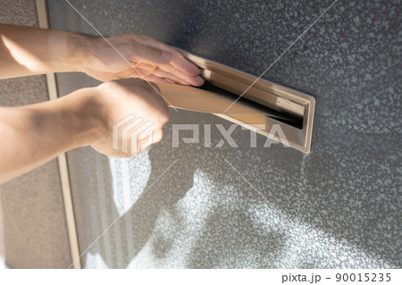 玄関の郵便受けに封筒を入れる手 90015235