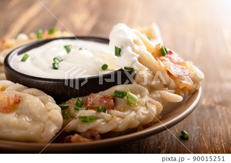 Potato dumplings with sour cream on the wooden table. Traditional ukrainian food. Varenyky, vareniki, pierogi, pyrohy - dumplings with filling. Potato dumplings with sour cream on the wooden table. Traditional ukrainian food. Varenyky, vareniki, pierogi, pyrohy - dumplings with filling. 90015251