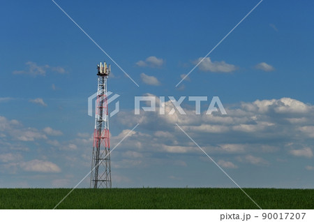 Telecommunication Tower - Transmitter for gsm signal of mobile phones in the field. In the background blue sky with clouds. Concept for modern technology and industry. Telecommunication Tower - Transmitter for gsm signal of mobile phones in the field. In the background blue sky with clouds. Concept for modern technology and industry. 90017207
