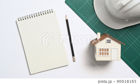 Above view blank notebook, house model and safety helmet on white table Above view blank notebook, house model and safety helmet on white table 90018165