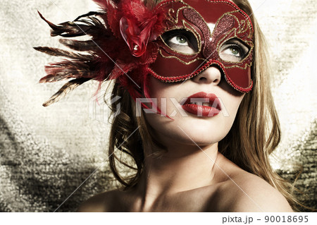 Beautiful young woman in a red mysterious venetian mask on a gold background 90018695