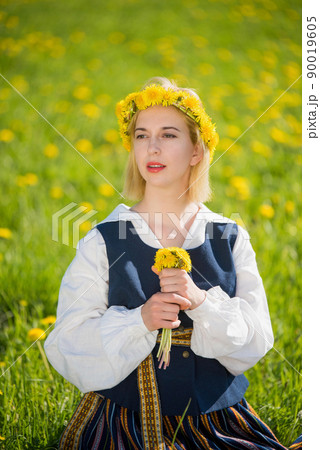Young woman in national clothes wearing yellow dandelion wreath in spring field. Ligo Young woman in national clothes wearing yellow dandelion wreath in spring field. Ligo 90019605