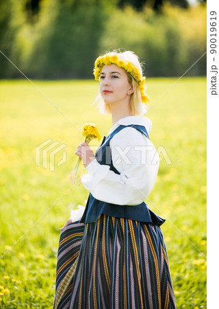 Young woman in national clothes wearing yellow dandelion wreath in spring field. Ligo Young woman in national clothes wearing yellow dandelion wreath in spring field. Ligo 90019619