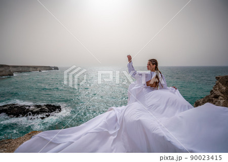 Happy freedom woman on the beach enjoying and posing in white dress. Rear view of a girl in a fluttering white dress in the wind. Holidays, holidays at sea. Happy freedom woman on the beach enjoying and posing in white dress. Rear view of a girl in a fluttering white dress in the wind. Holidays, holidays at sea. 90023415