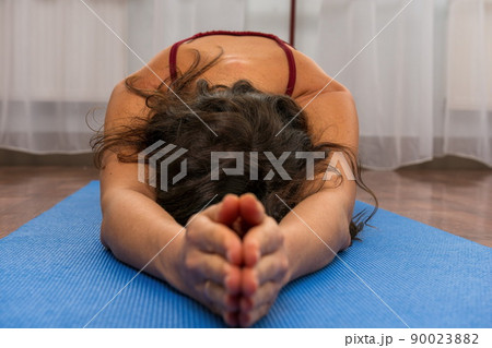 A young woman fitness instructor in red Sportswear Leggings and Top stretching in the gym before her pilates, on a yoga mat near the large window on a sunny day, female fitness yoga routine concept. A young woman fitness instructor in red Sportswear Leggings and Top stretching in the gym before her pilates, on a yoga mat near the large window on a sunny day, female fitness yoga routine concept. 90023882