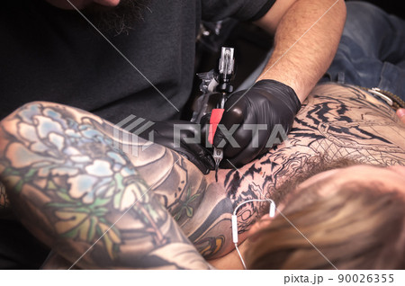 Professional tattoo artist makes a tattoo on the client's his salon 90026355