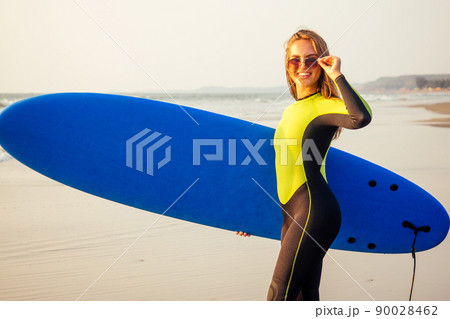 Young sexy woman wetsuit sportive body diving suit with surf board on the beach . Positive emotions cool surfing girl enjoying the summer moment of sunset on the paradise shore travel and impression Young sexy woman wetsuit sportive body diving suit with surf board on the beach . Positive emotions cool surfing girl enjoying the summer moment of sunset on the paradise shore travel and impression 90028462