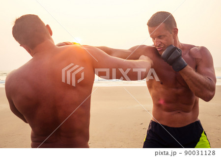 Strong boxer shirtless coach during kickboxing exercise with trainer in boxing gloves at sunset.sports figure, perfect abdominal muscles motivation Strong boxer shirtless coach during kickboxing exercise with trainer in boxing gloves at sunset.sports figure, perfect abdominal muscles motivation 90031128