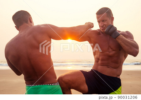 Strong boxer man doing during kickboxing exercise fight with trainer at sunset .close portrait of handsome fitness male model bodybuilder rage, anger and a splash of negative emotions 90031206