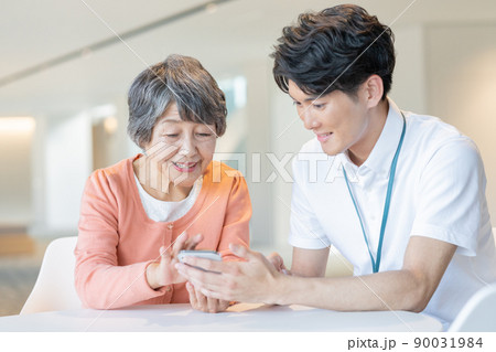 若い男性職員にスマホの操作を教わるシニア女性　撮影協力「LINK FOREST] 90031984