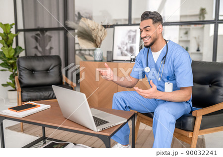 Joyful young doctor consulting his patient online 90032241
