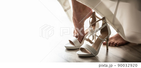 Bride puts her foot into white high heel shoe before the start of a wedding ceremony Bride puts her foot into white high heel shoe before the start of a wedding ceremony 90032920