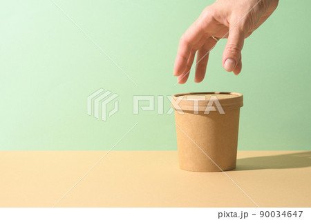 Craft paper soup cup and female hand on brown background. Ecological individual package. Zero Waste. 90034647