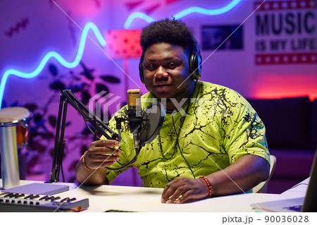 Young African American man wearing headphones adjusting microphone to start podcast or broadcast recording in home studio 90036028