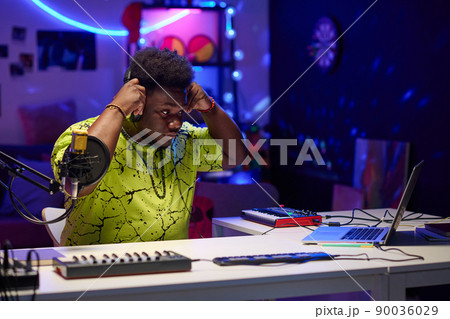 Portrait of young African American man wearing stylish neon T-shirt putting on headphones to start working on music track 90036029